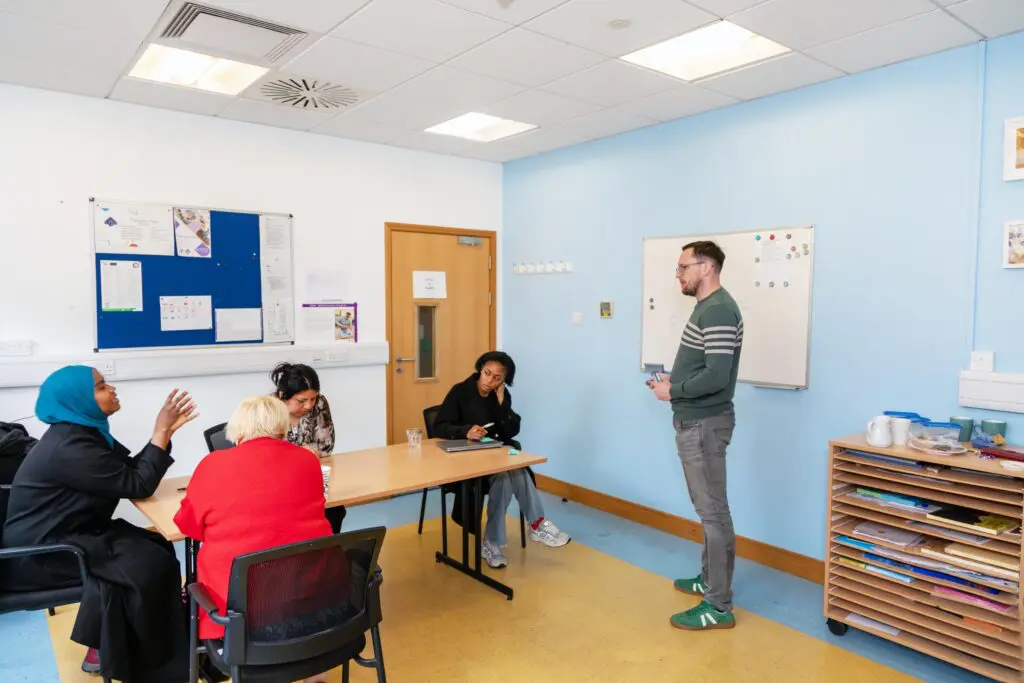 A diverse group of 4 learners discuss GCE with their facilitator in a classroom in the LYCS building. Photographed by Paul Reardon.