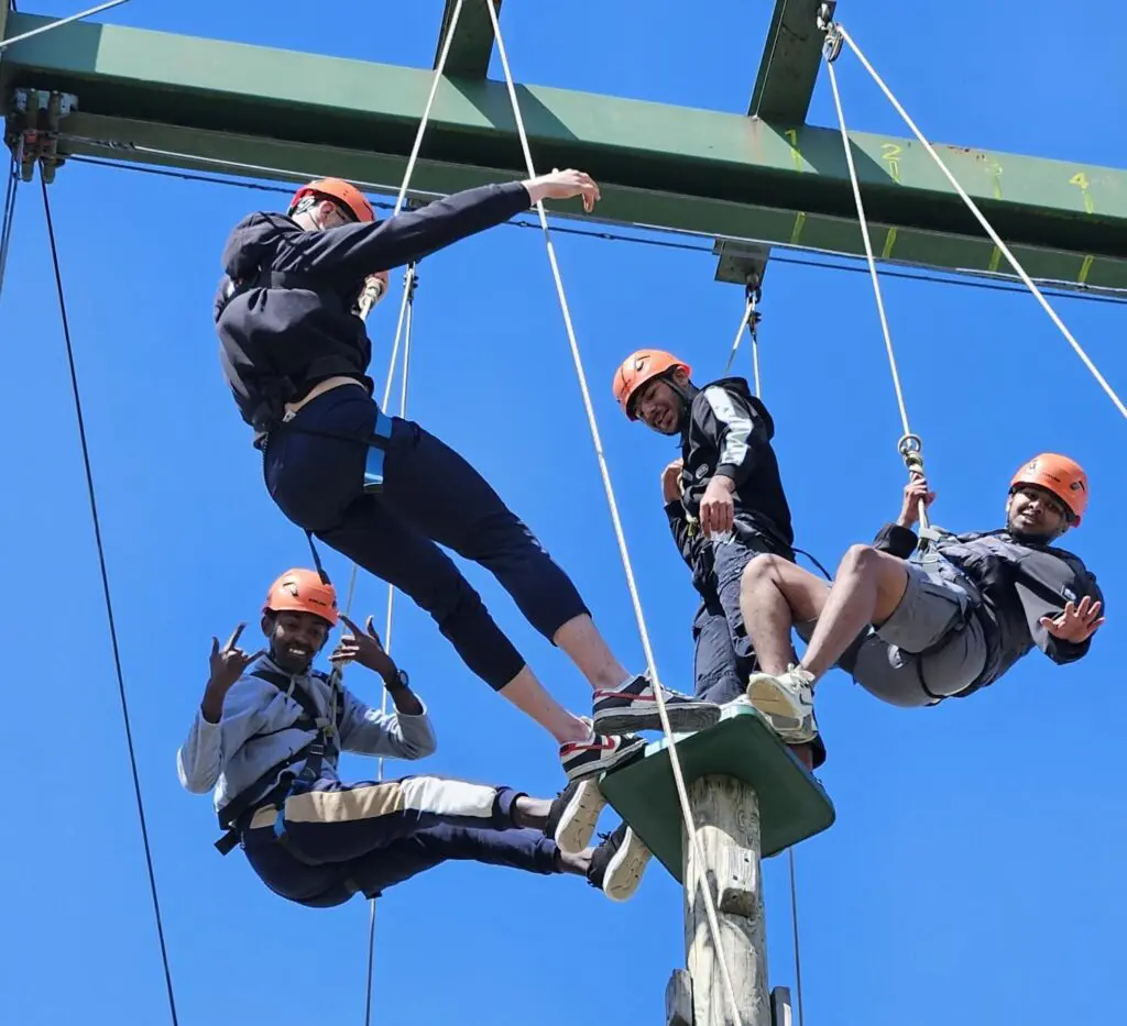 4 of our Gaisce participants balancing on a high stand in helmets and harnesses on abseiling ropes. There is a blue sky in the background.