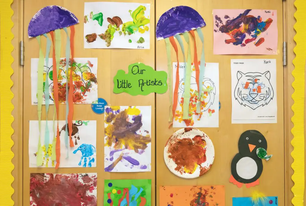 'Our Little Artists' wall in the creche. Displays jellyfish, jungle animals, and a penguin eating a fish. Abstract and colourful pictures are pinned amongst the animals. Photographed by Paul Reardon.