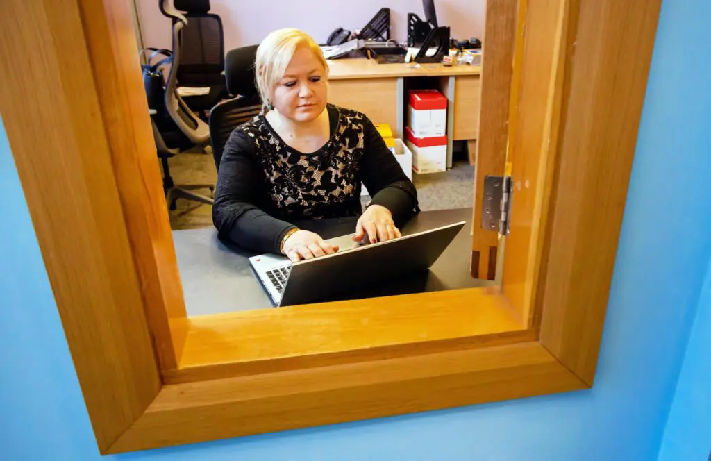 Our Community Employment participant is pictured through the reception window as she works on her laptop. Photographed by Paul Reardon.